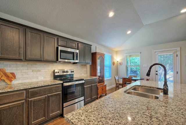 kitchen with light stone countertops, appliances with stainless steel finishes, tasteful backsplash, sink, and lofted ceiling