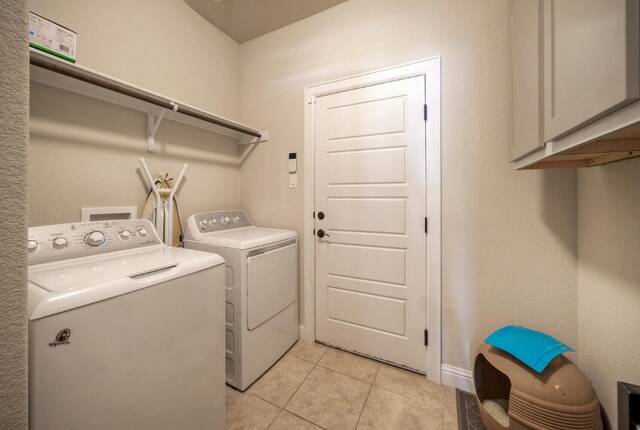 clothes washing area featuring washer and clothes dryer, light tile patterned flooring, and cabinets