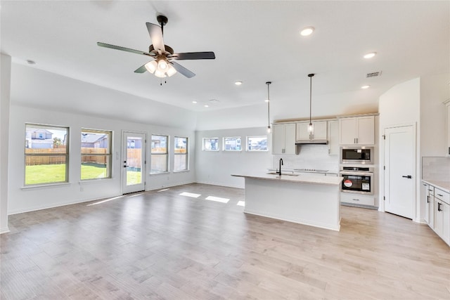 kitchen featuring stainless steel appliances, ceiling fan, light hardwood / wood-style floors, hanging light fixtures, and an island with sink