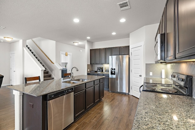 kitchen with appliances with stainless steel finishes, dark hardwood / wood-style flooring, a kitchen island with sink, and light stone counters