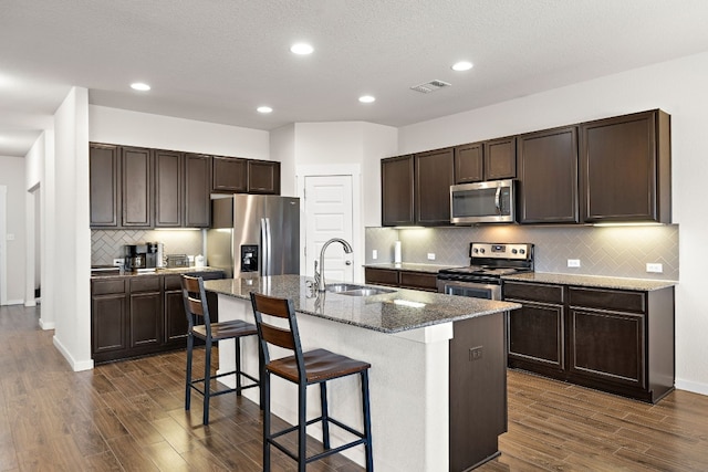 kitchen with stainless steel appliances, dark hardwood / wood-style flooring, sink, a center island with sink, and backsplash