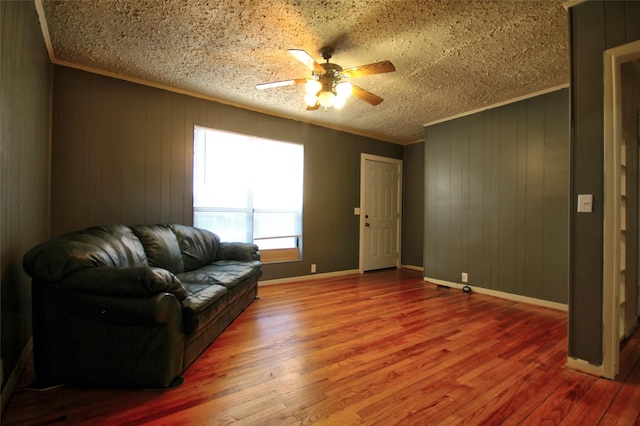 sitting room with crown molding, ceiling fan, wooden walls, and hardwood / wood-style floors