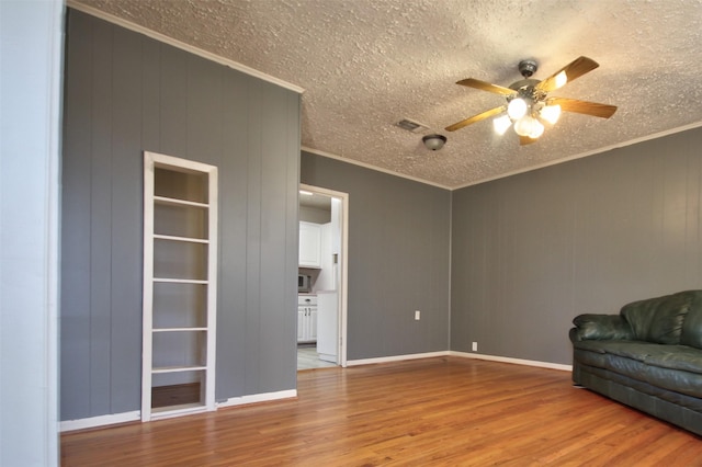 unfurnished living room featuring crown molding, ceiling fan, wooden walls, light hardwood / wood-style floors, and a textured ceiling