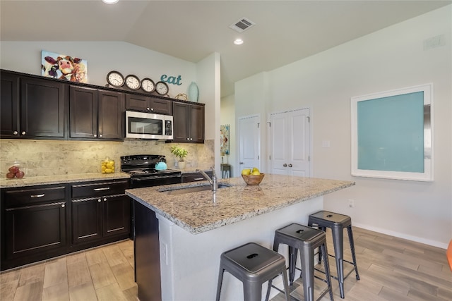 kitchen featuring lofted ceiling, black range with electric stovetop, an island with sink, light hardwood / wood-style flooring, and sink