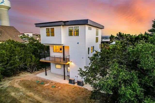 back house at dusk featuring a balcony and central air condition unit