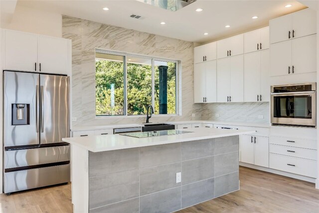 kitchen featuring white cabinets, sink, a kitchen island, appliances with stainless steel finishes, and light hardwood / wood-style flooring