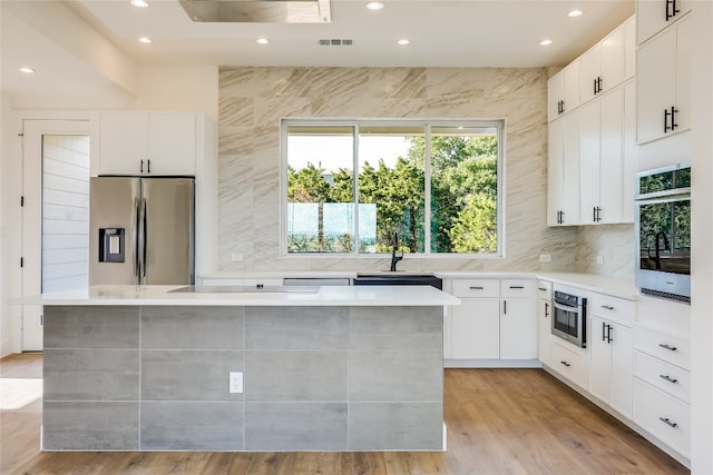 kitchen with white cabinets, a center island, light hardwood / wood-style floors, and appliances with stainless steel finishes