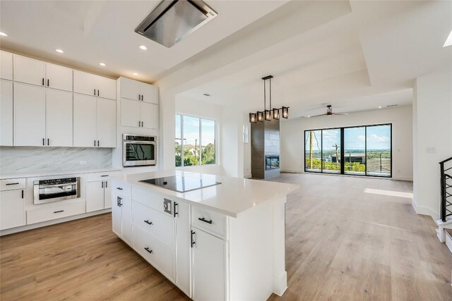 kitchen featuring black electric cooktop, stainless steel oven, a center island, light hardwood / wood-style floors, and decorative light fixtures