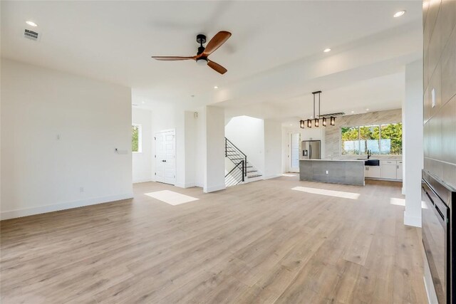 unfurnished living room featuring light hardwood / wood-style flooring, sink, and ceiling fan