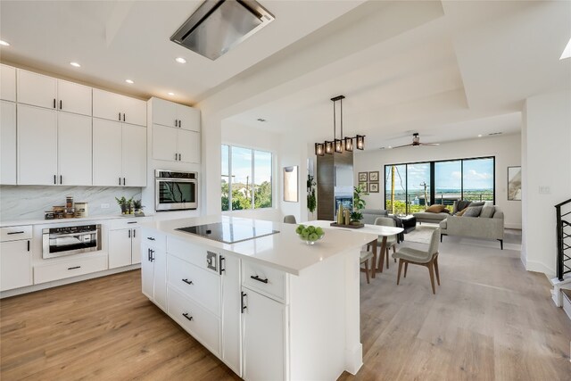 kitchen with black electric cooktop, white cabinets, oven, a kitchen island, and light hardwood / wood-style floors