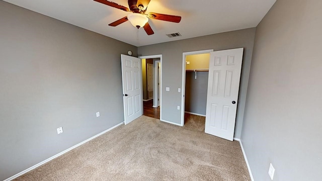 unfurnished bedroom with ceiling fan, light colored carpet, a closet, and a walk in closet