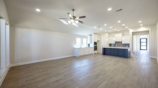 kitchen with white cabinets, vaulted ceiling, light wood-type flooring, and backsplash