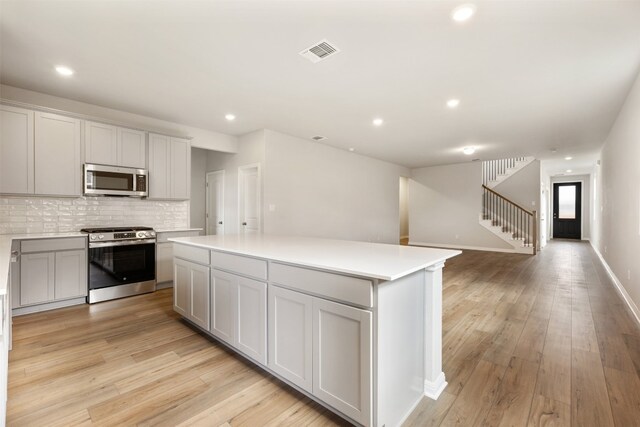 kitchen with light hardwood / wood-style floors, appliances with stainless steel finishes, backsplash, and a kitchen island