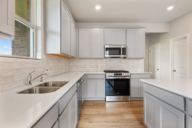 kitchen with tasteful backsplash, light hardwood / wood-style flooring, sink, gray cabinetry, and stainless steel appliances