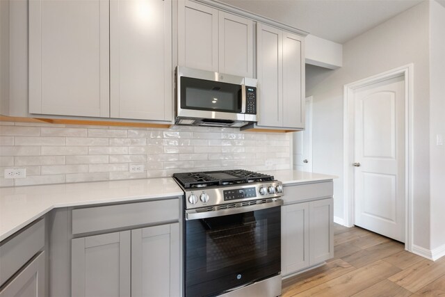 kitchen with light hardwood / wood-style floors, stainless steel appliances, gray cabinets, and backsplash