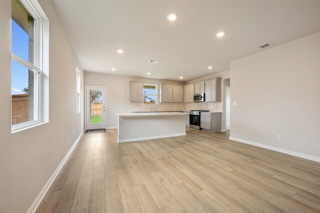 kitchen with gray cabinets, backsplash, appliances with stainless steel finishes, a kitchen island, and light hardwood / wood-style floors