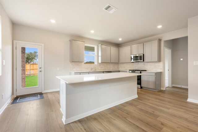 kitchen featuring a kitchen island, gray cabinetry, backsplash, appliances with stainless steel finishes, and light hardwood / wood-style floors