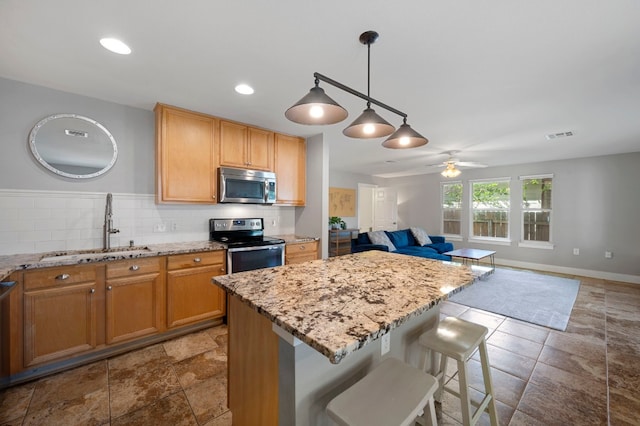 kitchen with tasteful backsplash, ceiling fan, a breakfast bar, sink, and appliances with stainless steel finishes