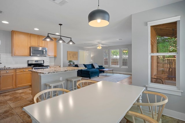 kitchen featuring a kitchen island, decorative light fixtures, stainless steel appliances, a kitchen breakfast bar, and ceiling fan