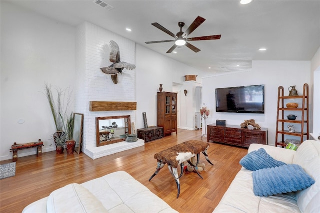 living room featuring vaulted ceiling, a brick fireplace, ceiling fan, and light wood-type flooring