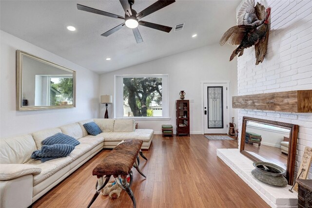 living room featuring ceiling fan, vaulted ceiling, wood-type flooring, and a brick fireplace