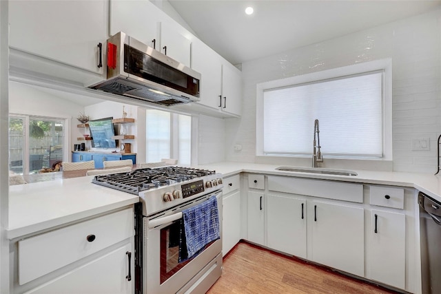 kitchen with vaulted ceiling, white cabinetry, sink, light hardwood / wood-style floors, and stainless steel appliances