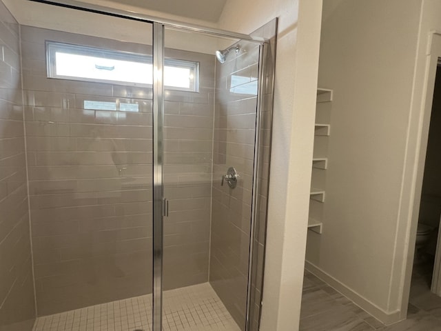 bathroom with tile patterned floors, a shower with door, toilet, and a wealth of natural light