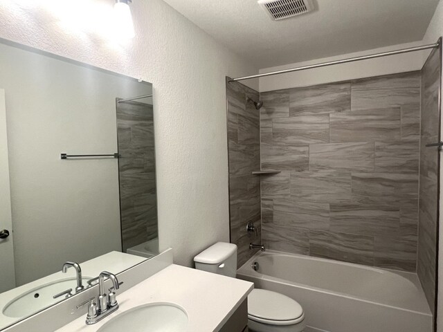 full bathroom with vanity, tiled shower / bath, a textured ceiling, and toilet