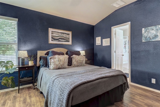 bedroom with multiple windows, ensuite bathroom, hardwood / wood-style floors, and vaulted ceiling