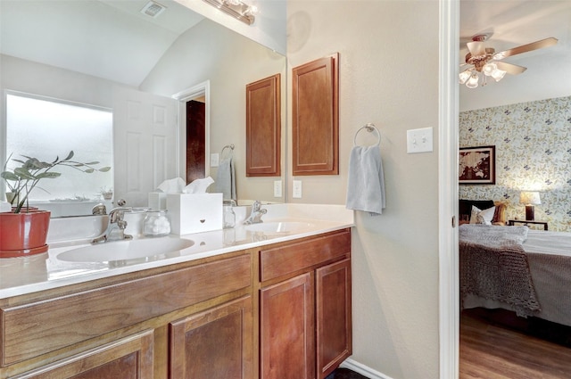 bathroom featuring dual bowl vanity, ceiling fan, a fireplace, wood-type flooring, and vaulted ceiling