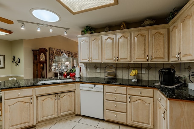 kitchen featuring light tile patterned flooring, dark stone counters, white dishwasher, decorative backsplash, and sink