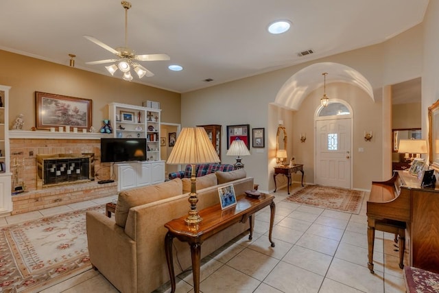 tiled living room featuring crown molding, a brick fireplace, and ceiling fan