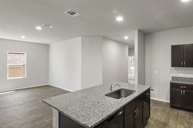 kitchen with dark wood-type flooring, light stone counters, dishwasher, a center island with sink, and sink