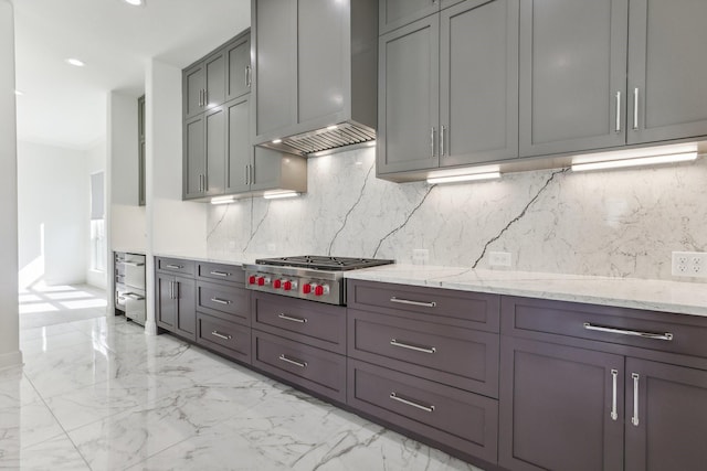 kitchen featuring gray cabinets, tasteful backsplash, light stone countertops, stainless steel gas cooktop, and wall chimney exhaust hood