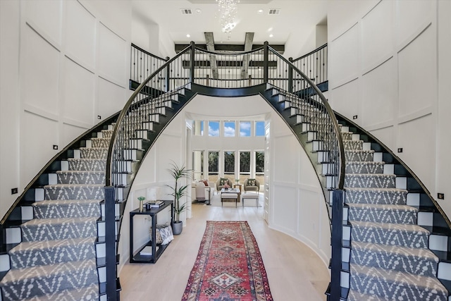 staircase with a towering ceiling, hardwood / wood-style floors, and a notable chandelier