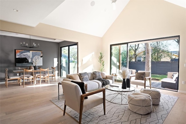 living room with high vaulted ceiling, light wood-type flooring, and an inviting chandelier