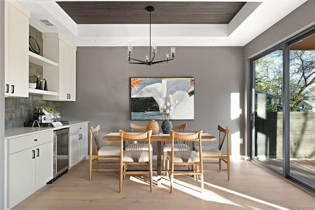 dining space with wine cooler, a notable chandelier, light hardwood / wood-style flooring, and a raised ceiling