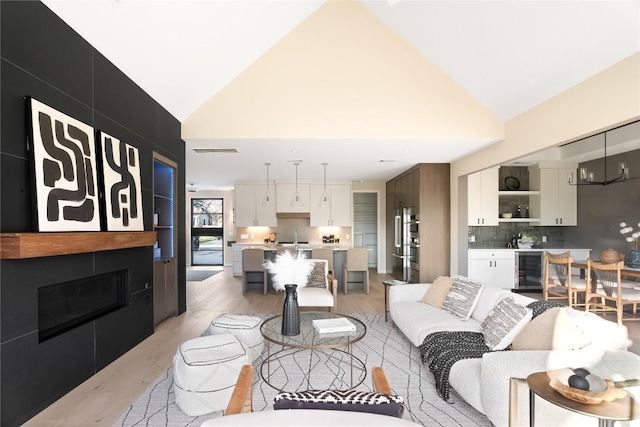 living room with sink, high vaulted ceiling, wine cooler, a fireplace, and light wood-type flooring