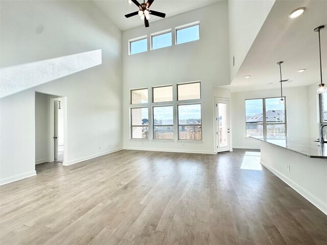 unfurnished living room featuring baseboards, a high ceiling, ceiling fan, and wood finished floors