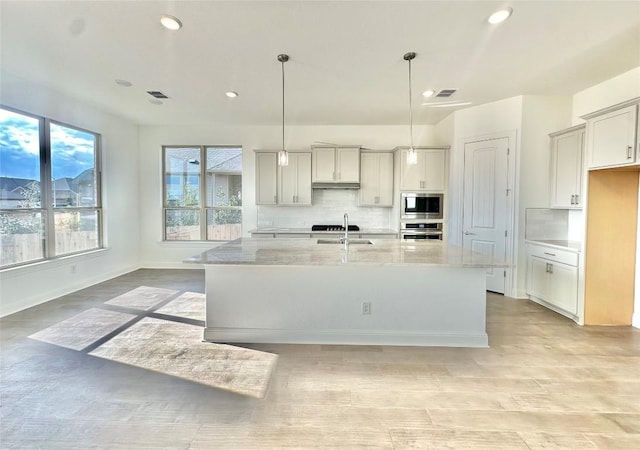 kitchen with visible vents, a sink, appliances with stainless steel finishes, decorative backsplash, and light stone countertops