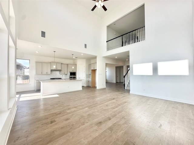 unfurnished living room featuring ceiling fan, visible vents, light wood-style flooring, and stairway