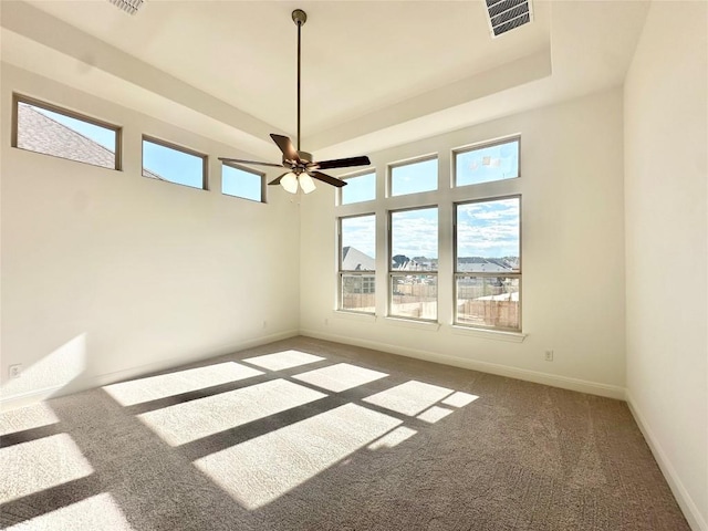 carpeted empty room with a tray ceiling, visible vents, baseboards, and ceiling fan