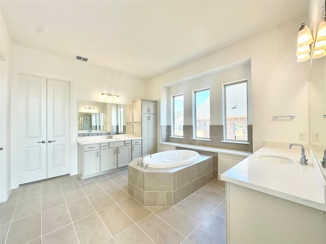 bathroom with visible vents, two vanities, a sink, tile patterned flooring, and a bath