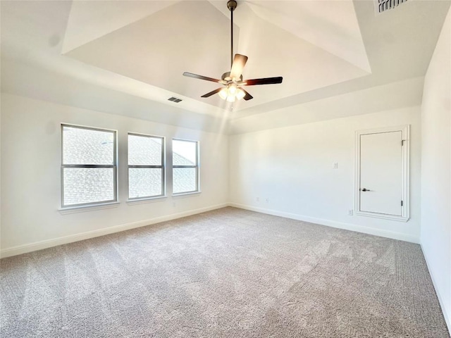 empty room featuring baseboards, a tray ceiling, light carpet, and visible vents