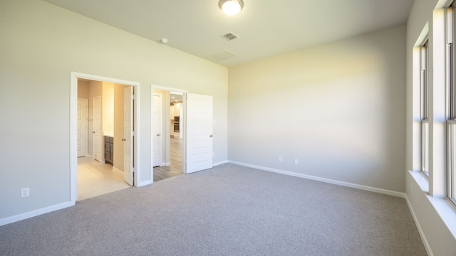 unfurnished bedroom featuring connected bathroom and light carpet