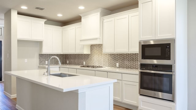 kitchen with stainless steel appliances, a center island with sink, white cabinets, sink, and light hardwood / wood-style flooring