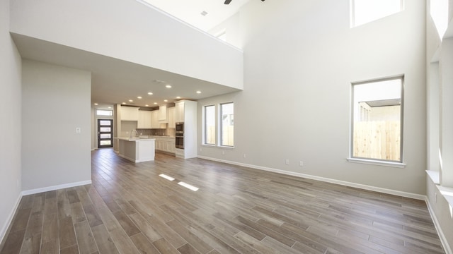 unfurnished living room featuring a high ceiling, ceiling fan, and light hardwood / wood-style floors