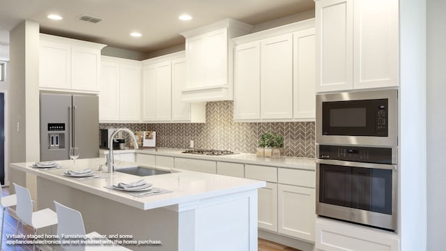 kitchen with white cabinetry, appliances with stainless steel finishes, sink, and an island with sink