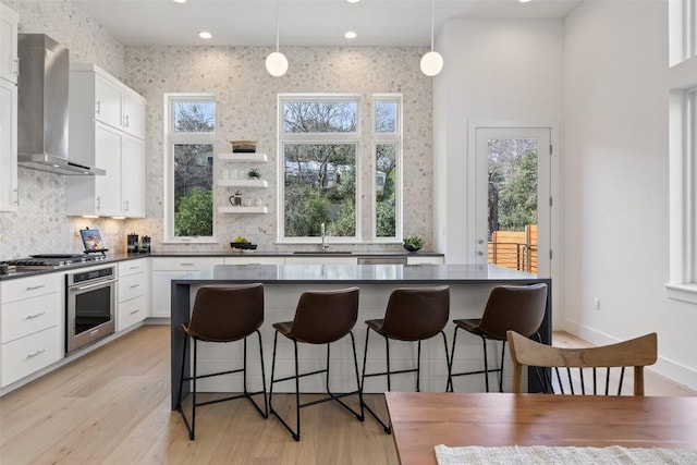 kitchen with stainless steel appliances, white cabinets, wall chimney range hood, pendant lighting, and sink