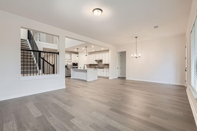 unfurnished living room featuring a notable chandelier, sink, and light wood-type flooring